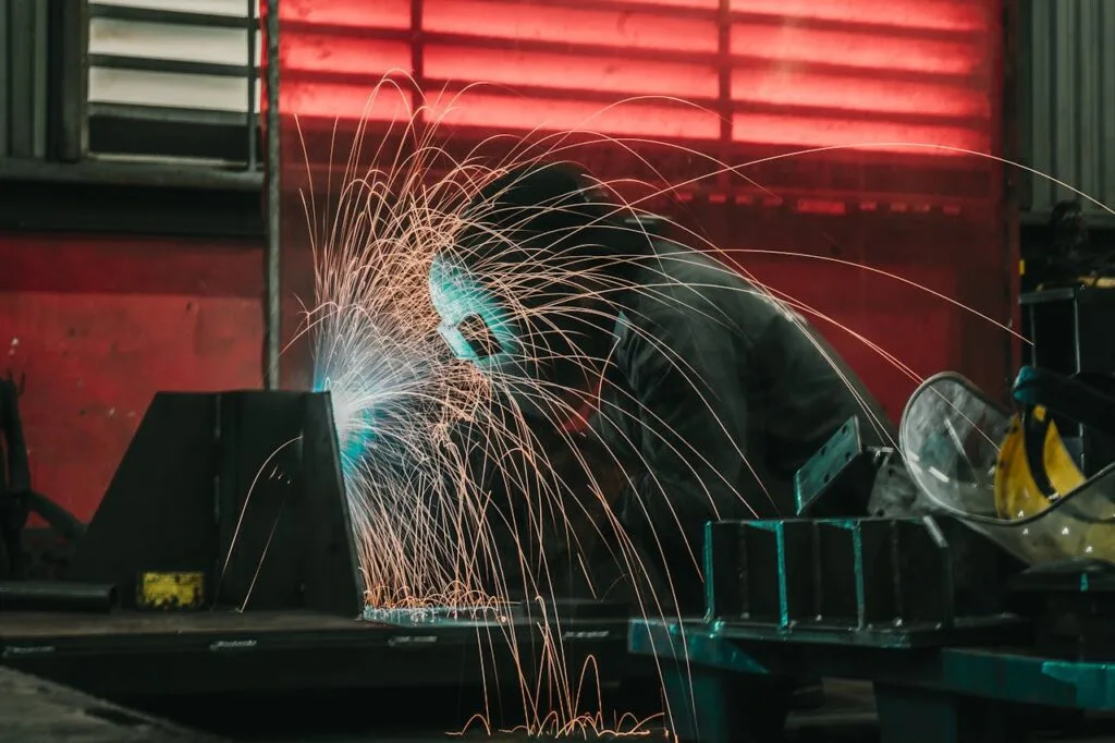 A welder skillfully creates sparks while working in an industrial workshop, wearing protective gear.